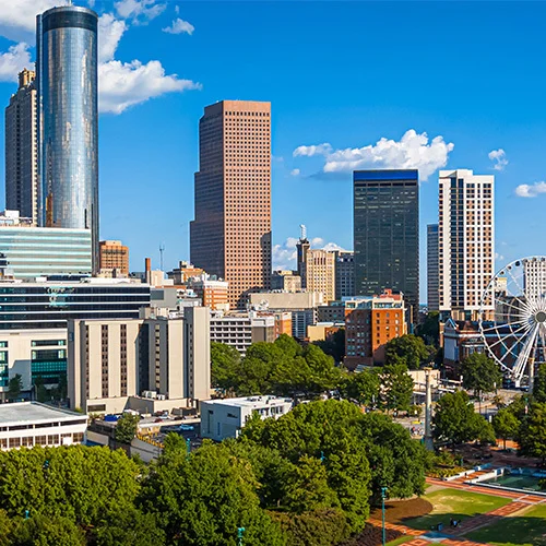 Atlanta skyline overlooking Centennial Olympic Park, featuring modern skyscrapers, green lawns, walking paths, and the Ferris wheel on a sunny day.