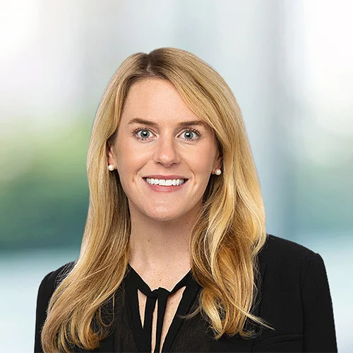Professional headshot of Lea McBryde with shoulder-length blonde hair wearing a black blazer and black top, facing forward against a softly blurred, neutral-toned background.