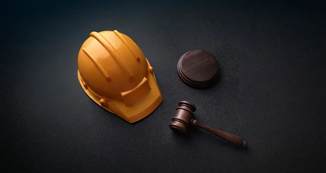 Yellow construction hard hat placed beside a wooden gavel and sound block on a dark surface, symbolizing the intersection of construction and legal matters.
