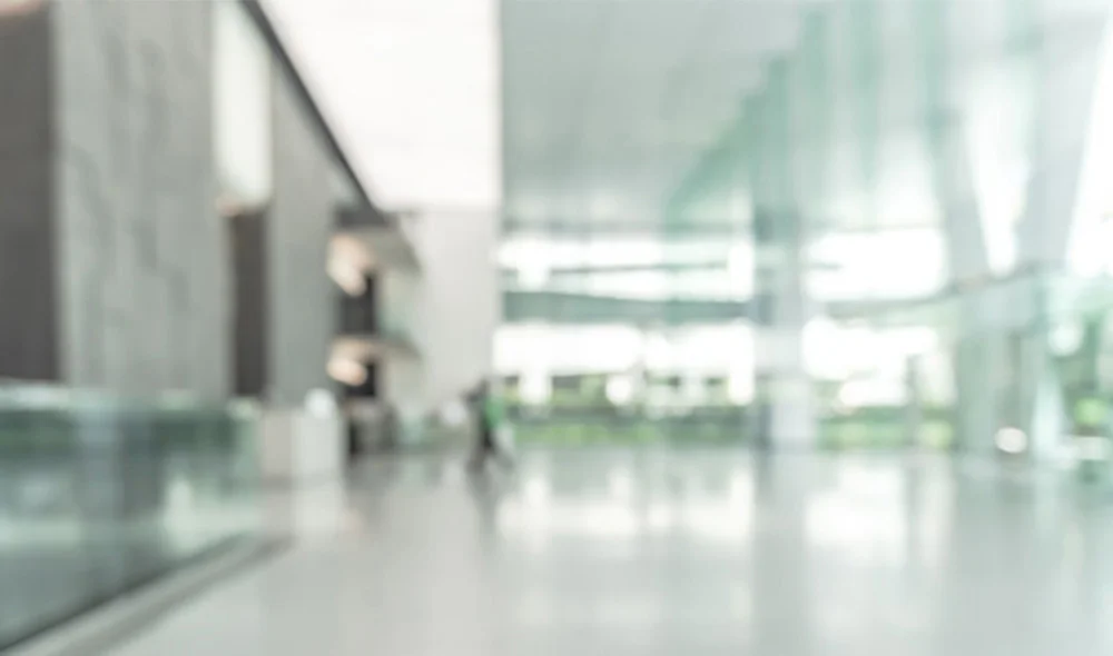 Bright, modern office lobby with tall glass windows and a polished floor, softly blurred to create an abstract, minimalist background with natural light.