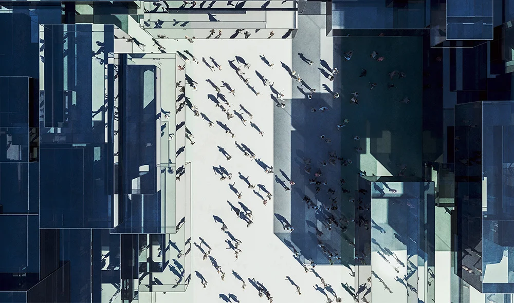 Overhead view of a modern urban plaza with geometric architectural structures casting shadows, where numerous people walk across an open space, creating patterns of movement and contrast between light and shade.